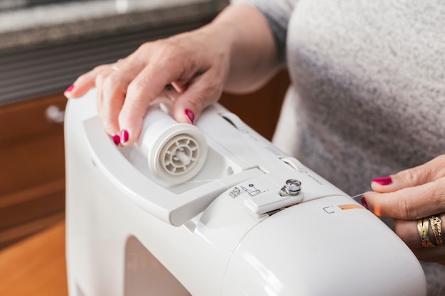 Primer plano de una mujer que ajusta el carrete de hilo en la máquina de coser