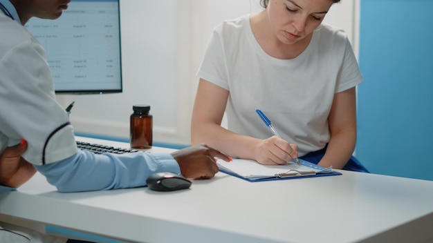 Primer plano de una mujer que firma documentos de chequeo para recibir tratamiento de un especialista. Médico que solicita la firma en los documentos de prescripción del paciente enfermo en la visita médica. Persona y médico con archivos.