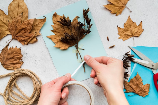 Primer plano de una mujer que pega las hojas de otoño con cinta blanca sobre fondo texturizado