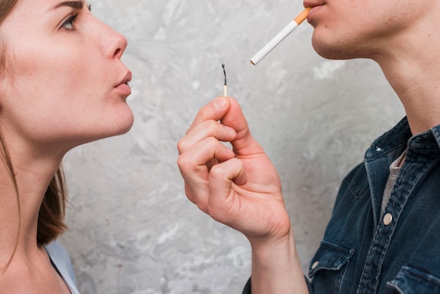 Primer plano de mujer que sopla partido palo mantenga por su novio llevando cigarrillos en la boca