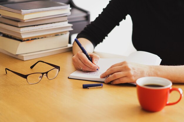 Primer plano de una mujer que trabaja o estudia desde casa con una taza de café roja cerca