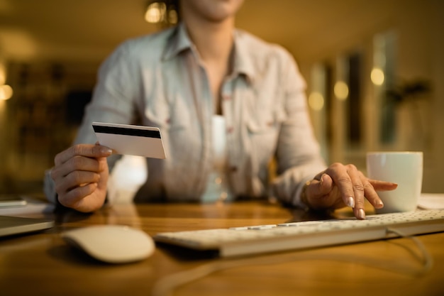 Primer plano de una mujer que usa una computadora y una tarjeta de crédito para la banca en línea por la noche en casa