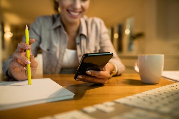 Primer plano de una mujer que usa un teléfono inteligente mientras aprende por la noche en casa