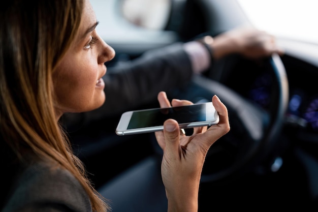 Primer plano de una mujer que usa un teléfono móvil y habla por el altavoz mientras conduce un automóvil