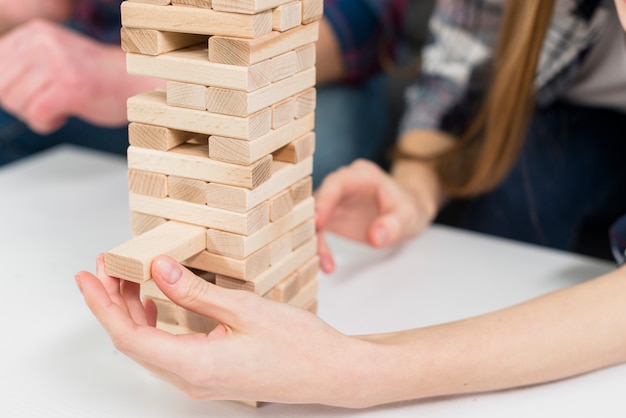 El primer plano de la mujer quita con cuidado un bloque de la torre de madera desordenada