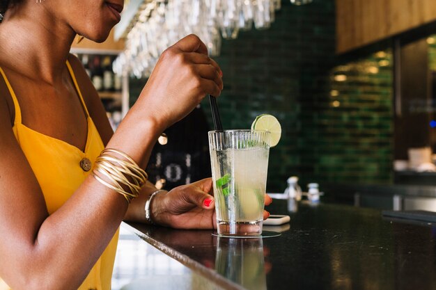 Primer plano de mujer revolviendo un mojito en barra de bar