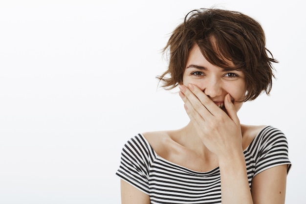 Primer plano de mujer riendo despreocupada, cerrar la boca con la mano y reír alegremente