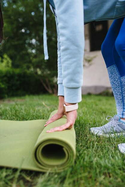 Primer plano de mujer rodillo plegable fitness o esterilla de yoga después de hacer ejercicio en el parque