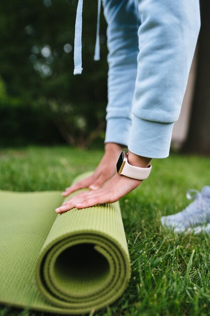 Primer plano de mujer rodillo plegable fitness o esterilla de yoga después de hacer ejercicio en el parque