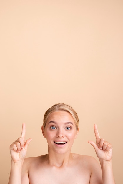 Primer plano mujer rubia sonriente apuntando hacia arriba