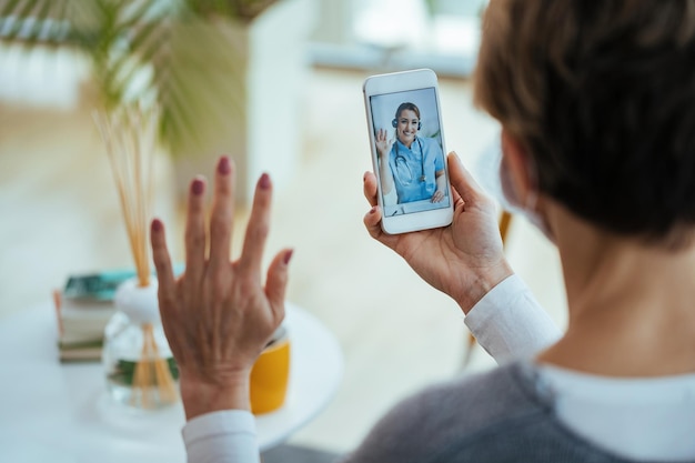 Primer plano de una mujer saludando a su médico mientras usa un teléfono inteligente y tiene una videollamada El foco está en la doctora en la pantalla táctil