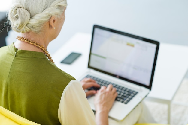 Primer plano de mujer senior escribiendo en la computadora portátil