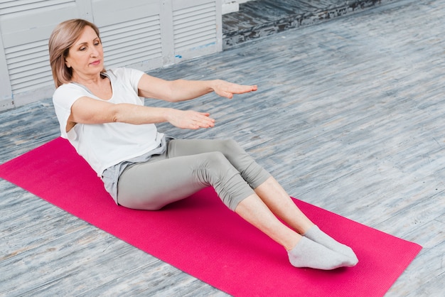 Primer plano de mujer senior estirando para tocar los dedos del pie mientras está sentado en la estera de yoga