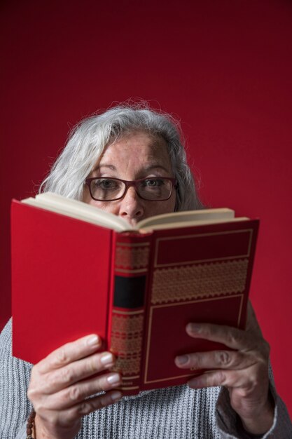 Primer plano de una mujer senior leyendo el libro sobre fondo rojo