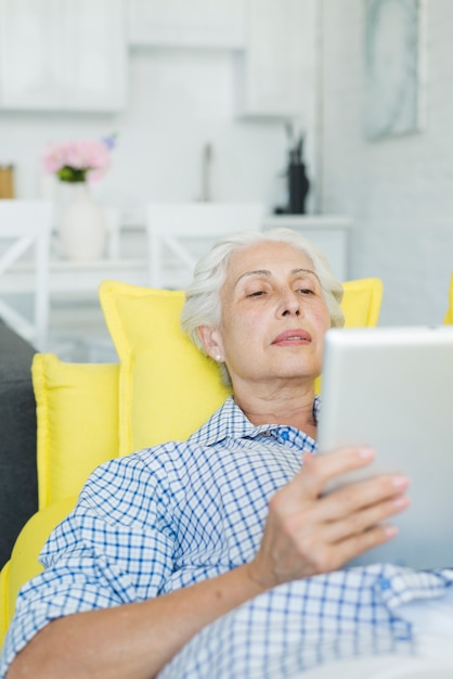 Primer plano de mujer senior relajante en sofá mirando tableta digital