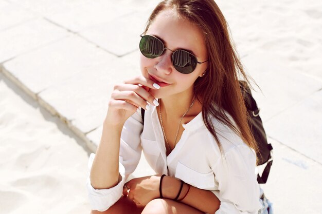 Primer plano de mujer sensual con gafas de sol sentada en la playa