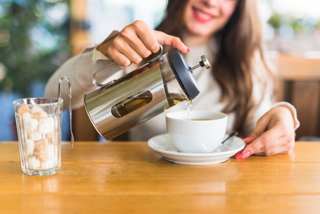 Primer plano de una mujer sentada en la mesa vertiendo té en la taza