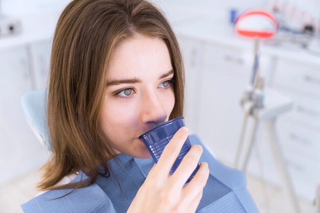 Primer plano de una mujer en silla dental tomar vaso de agua