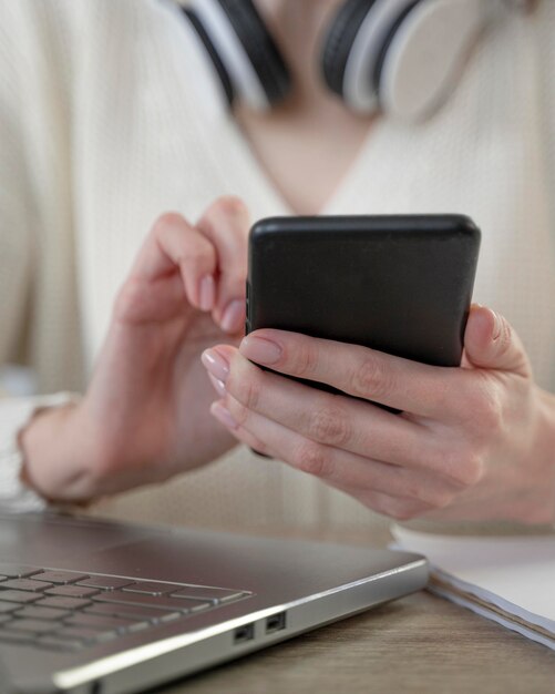 Primer plano de mujer con smartphone junto a la computadora portátil