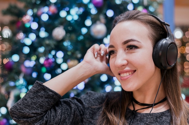 Primer plano de mujer sonriente con auriculares cerca de árbol de Navidad