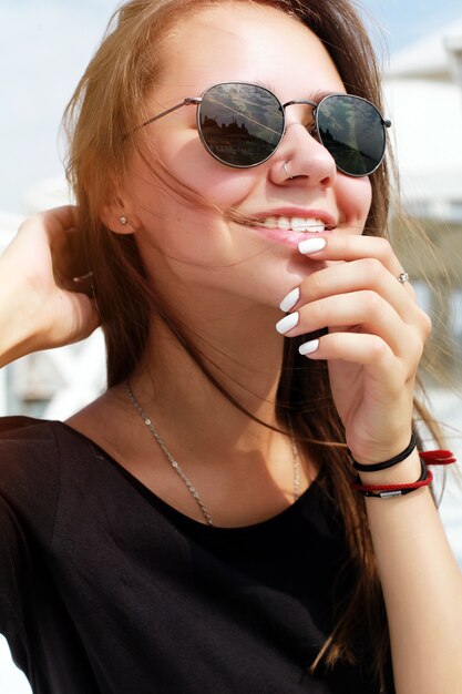 Primer plano de mujer sonriente con gafas de sol y tocándose la barbilla