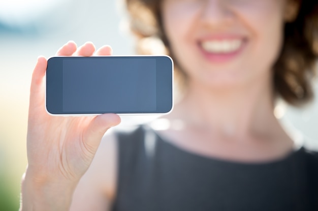 Primer plano de mujer sonriente mostrando un móvil