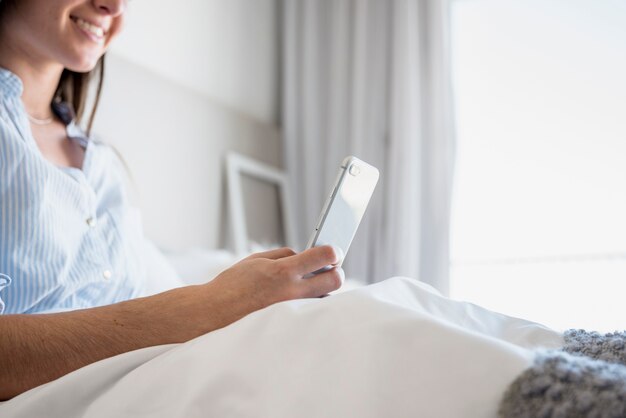 Primer plano de mujer sonriente sentada en la cama usando tableta digital