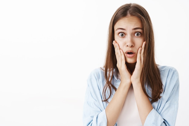 Primer plano de una mujer sorprendida que expresa empatía, escuchando noticias aterradoras e impresionantes, labios doblados con las palmas de las manos en la cara mirando asombrado y sin palabras