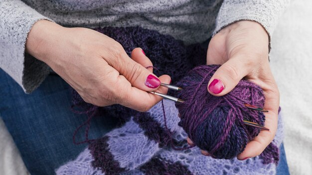 Primer plano de una mujer sosteniendo agujas de punto y bola de lana púrpura