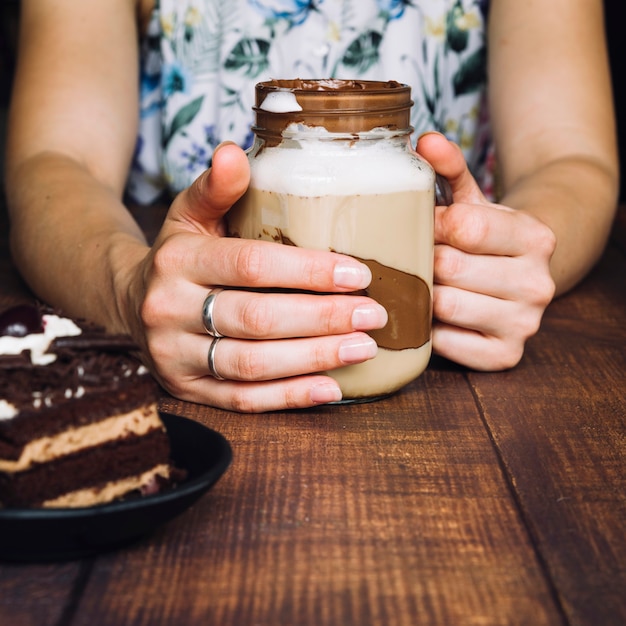 Primer plano de mujer sosteniendo el batido de chocolate en el vaso en la mesa de madera