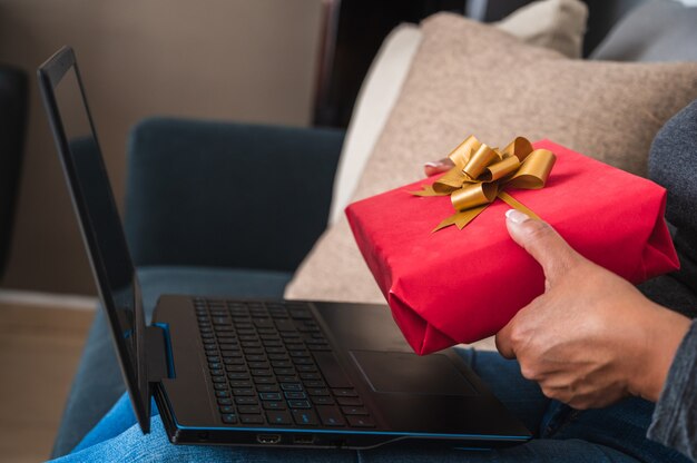 Primer plano de una mujer sosteniendo una caja de regalo roja delante de su computadora portátil