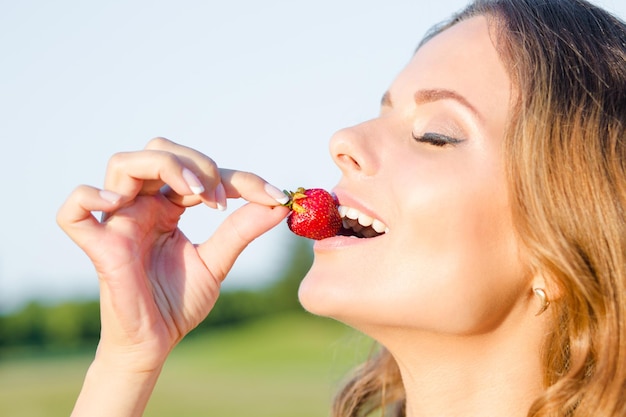 Primer plano de mujer sosteniendo y comiendo una cereza roja. Primer plano de una chica sensual con piel delicada jugando con una cereza.