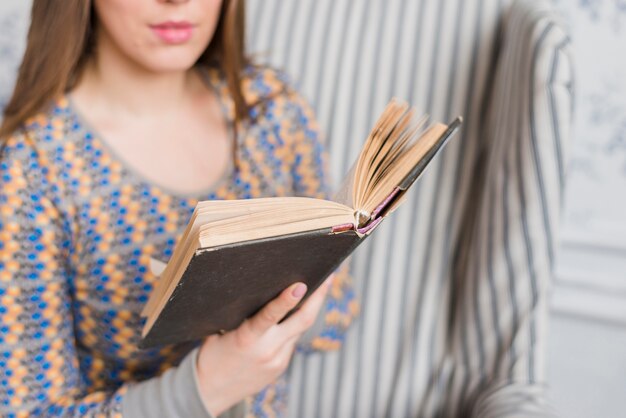 Primer plano de una mujer sosteniendo un libro en manos sentado en un sillón