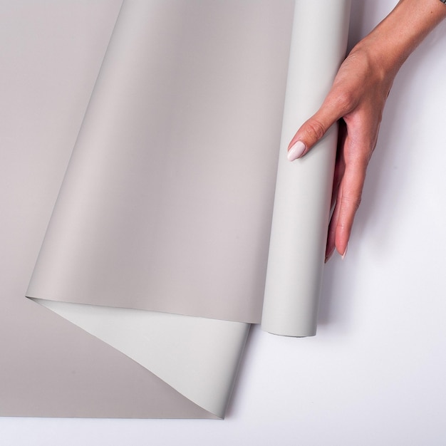 Primer plano de una mujer sosteniendo un rollo de papel tapiz gris sobre un fondo blanco.