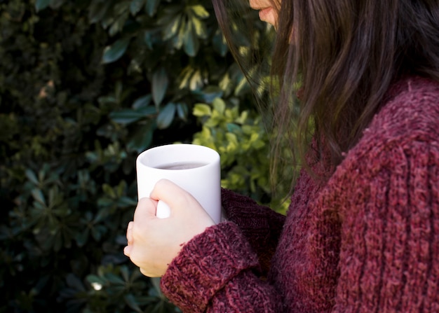 Primer plano de una mujer sosteniendo la taza de té de hierbas blancas