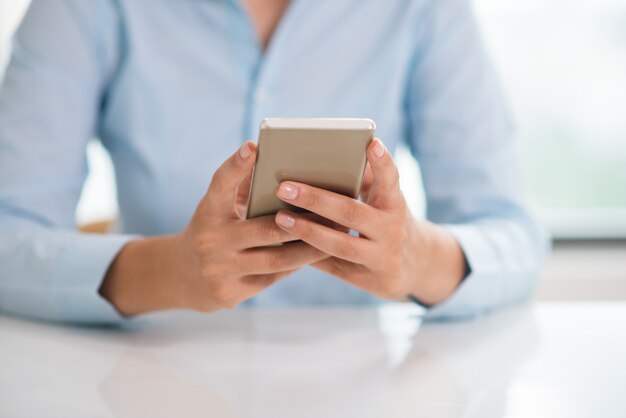 Primer plano de mujer sosteniendo y usando teléfono inteligente en la mesa