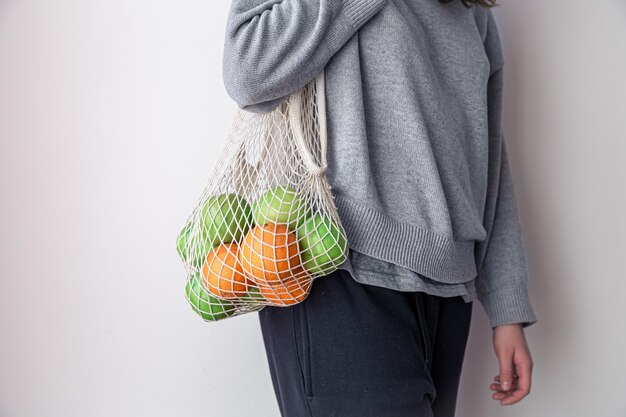 Primer plano una mujer sostiene una bolsa de hilo con manzanas y naranjas
