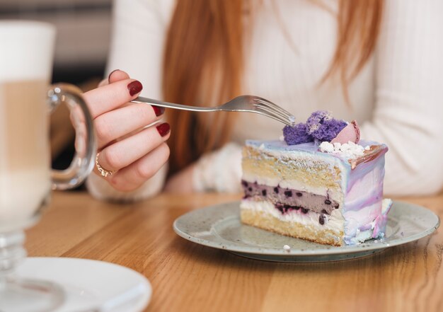 Primer plano de una mujer con un tenedor sobre la deliciosa rebanada de pastel de arándanos en un plato sobre la mesa de madera