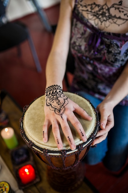 Primer plano de una mujer tocando el bongo drum con tatuaje mehndi en su mano