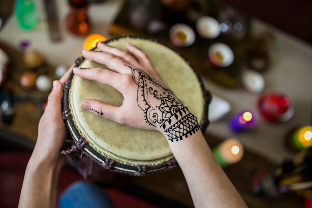 Primer plano de mujer tocando tambor con tatuaje mehndi en su mano