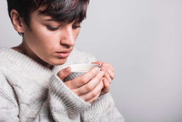 Primer plano de mujer tomando café contra el fondo gris