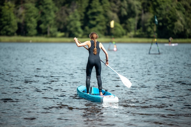 Primer plano de una mujer en un traje deportivo negro remando en un lago en competición de sup