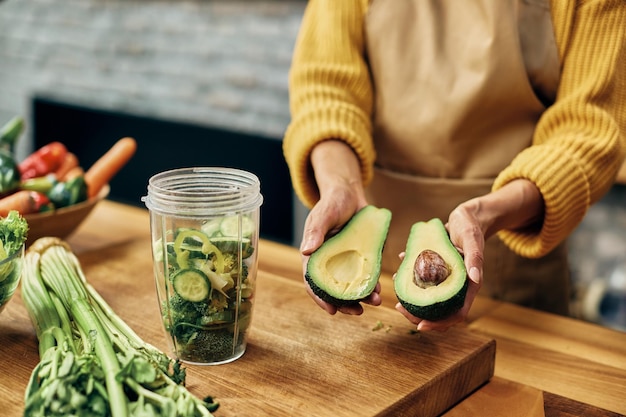 Primer plano de una mujer usando aguacate mientras prepara un batido de desintoxicación en la cocina