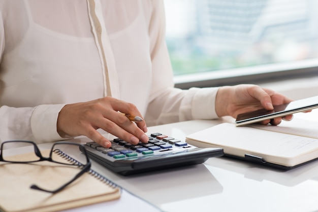 Primer plano de mujer usando calculadora y teléfono inteligente