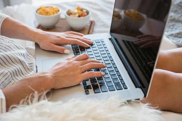 Primer plano de una mujer usando una computadora portátil con desayuno en la cama