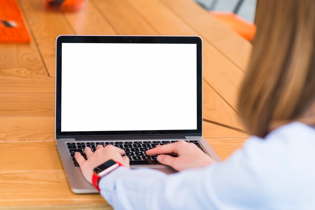 Primer plano de una mujer usando una computadora portátil con pantalla blanca en blanco sobre un escritorio de madera