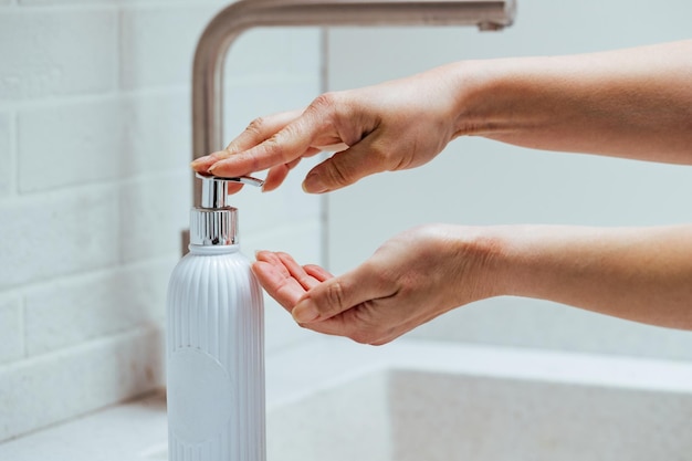 Primer plano de una mujer usando un dispensador de jabón y lavándose las manos en el baño