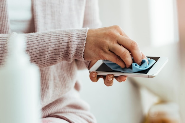 Primer plano de una mujer usando un paño de tela mientras limpia su teléfono inteligente en casa