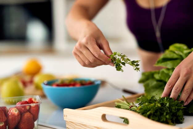 Primer plano de una mujer usando perejil mientras prepara alimentos saludables en la cocina