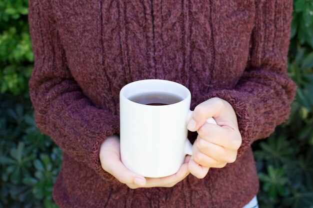 Primer plano de una mujer vestida con suéter de lana sosteniendo una taza de té de hierbas